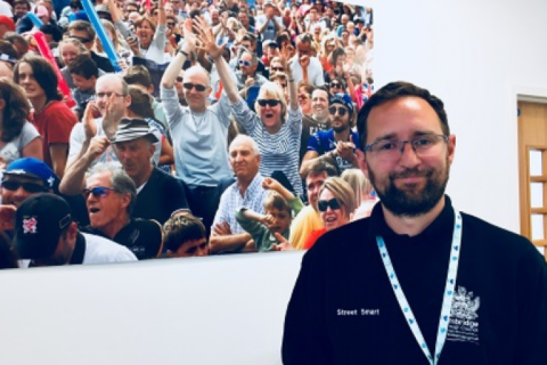 Martin Kearton smiling in front of an image on the wall of a group of people