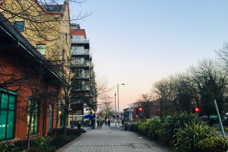 A pathway in Walton-on-Thames lined with flats and next to a nearby road in the evening