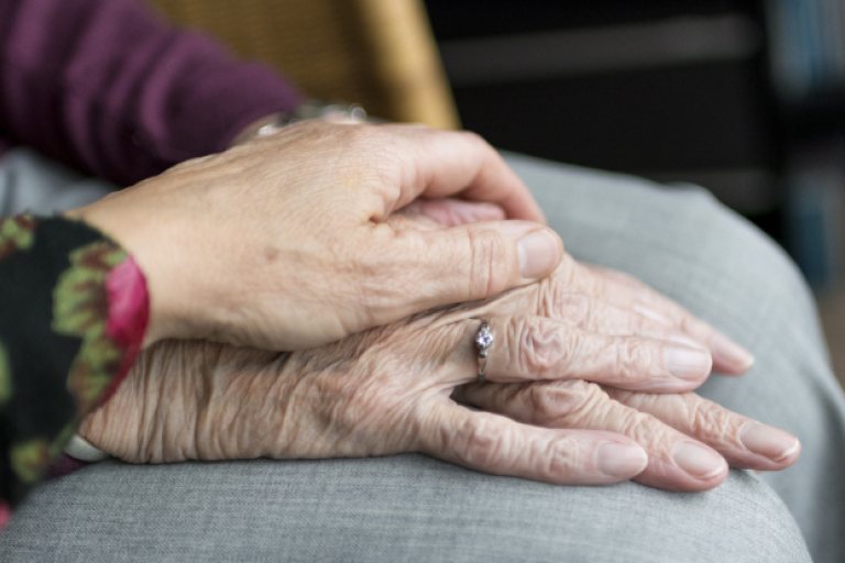 Woman's hand placed on top of an elderly woman's hands rested on her lap