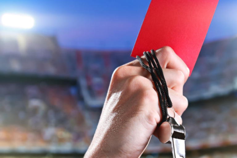 Hand holding red card and whistle in a stadium setting