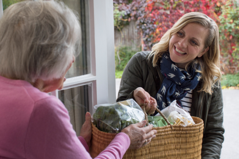 Woman handing over a basket of food to another woman on a doorstep