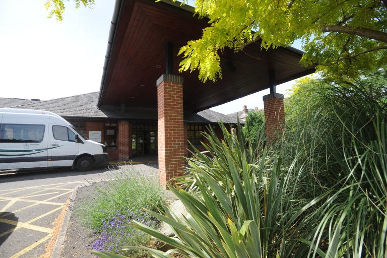 Entrance of Claygate Centre for the Community with greenery and Community Transport bus outside