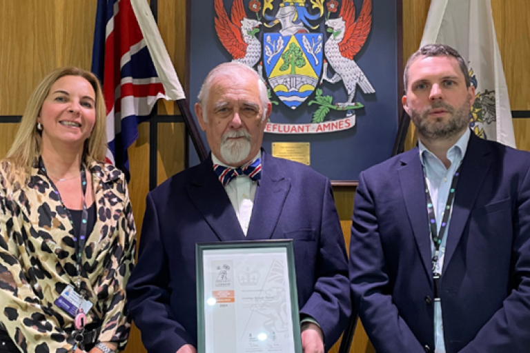 Representatives standing in front of council crest with bronze award