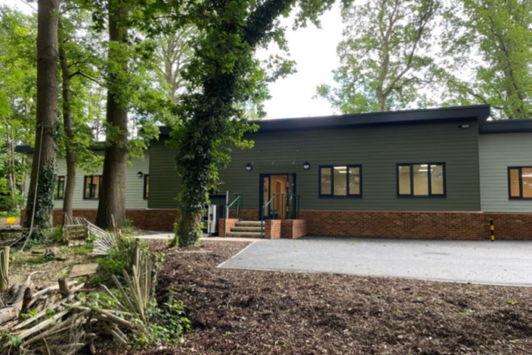 Green panelled building surrounded by woodchip and leafy green trees