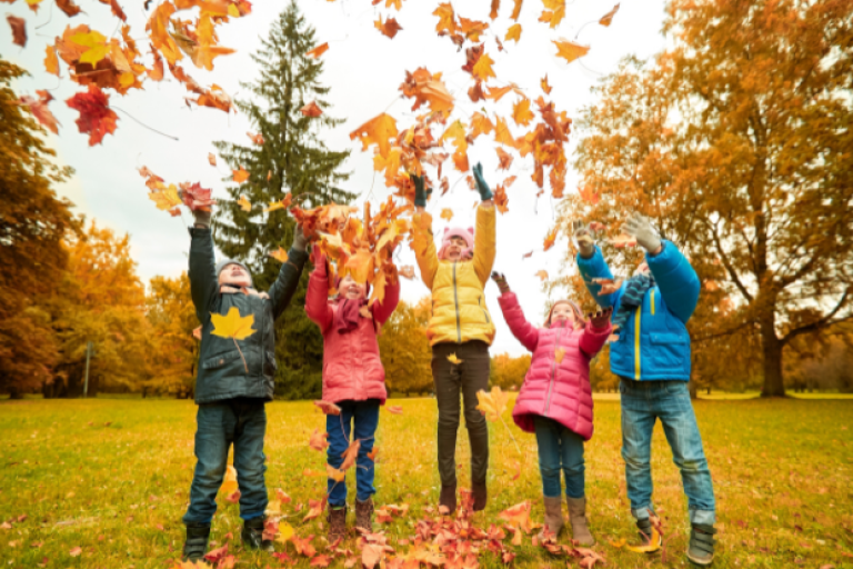 Children throwing orange autumnal leaves into the air and jumping