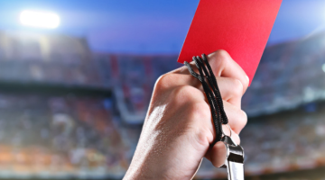 Hand holding red card and whistle in a stadium setting