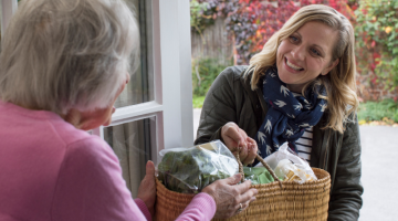 Woman handing over a basket of food to another woman on a doorstep