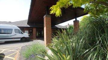 Entrance of Claygate Centre for the Community with greenery and Community Transport bus outside