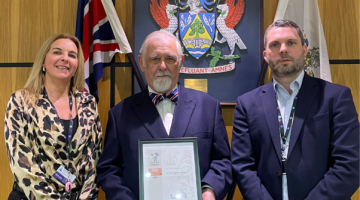 Representatives standing in front of council crest with bronze award